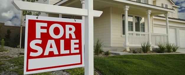 A white house with a red "For Sale" sign in front