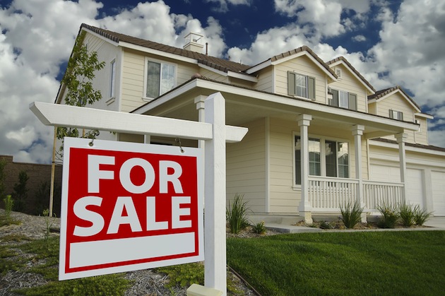 A white house with a red "For Sale" sign in front