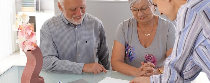 A smiling senior couple about to sign a form sitting at a desk with a young woman explaining to them