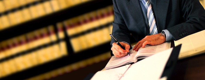 Lawyer at a desk writing with books in background and open on desk