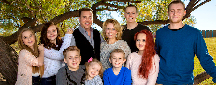 Portrait of a large family at the park under a tree. Parents with their eight children. Three brothers and fours sisters makes for lots of siblings.